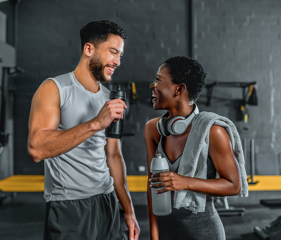 Two people in a gym setting, one holding a water bottle and the other a towel.